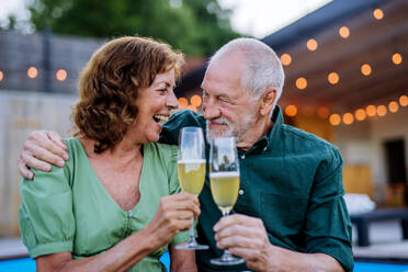 A man with number 70 balloons with his wife celebrating birthday and toasting with wine near backyard pool. - HPIF10971