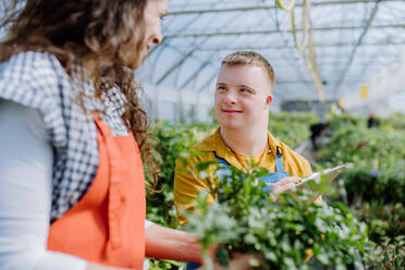 Eine erfahrene Floristin hilft einem jungen Mitarbeiter mit Down-Syndrom in einem Gartencenter. - HPIF10982