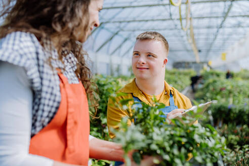 An experienced woman florist helping young employee with Down syndrome in garden centre. - HPIF10982