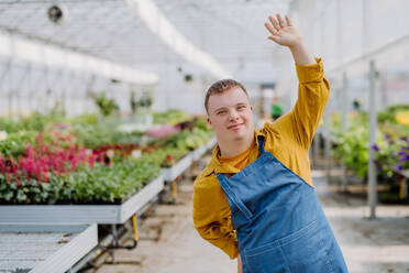 Ein junger Angestellter mit Down-Syndrom arbeitet in einem Gartencenter, schaut in die Kamera und winkt. - HPIF11009