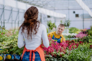 Eine erfahrene Floristin hilft einem jungen Mitarbeiter mit Down-Syndrom in einem Gartencenter. - HPIF11022