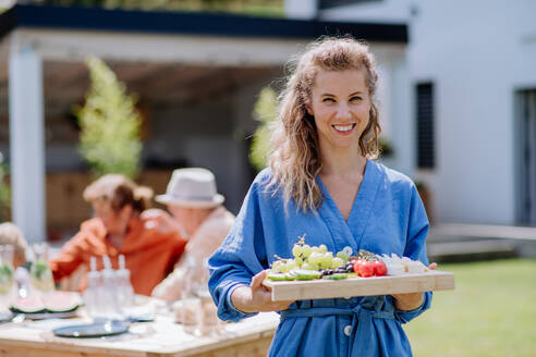 Porträt einer jungen Frau, die ein Tablett mit einem Snack für eine Gartenparty hält. - HPIF11051