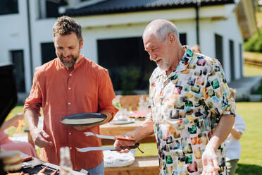 Ein älterer Vater mit erwachsenem Sohn grillt draußen im Hinterhof im Sommer Familie während Gartenparty - HPIF11052