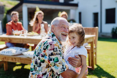 A happy little girl giving birthday present to her senior grandfather at generation family birthday party in summer garden - HPIF11054