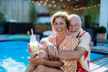 A happy senior couple enjoying drinks when relaxing and sitting by swimming pool in summer. - HPIF11058