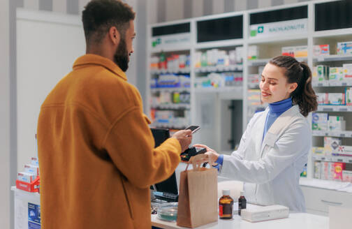 Junger multirassischer Mann beim Bezahlen von Medikamenten in einer Apotheke. - HPIF11092