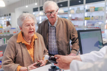 Junge Apothekerin verkauft Medikamente an ein älteres Ehepaar in einer Apotheke. - HPIF11110