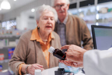 Junge Apothekerin verkauft Medikamente an ein älteres Ehepaar in einer Apotheke. - HPIF11111