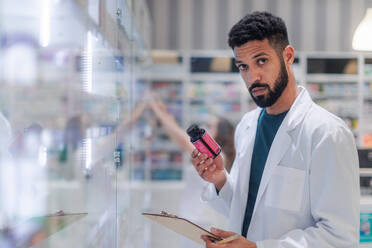 Young pharmacist checking medicine stock in a pharmacy. - HPIF11116
