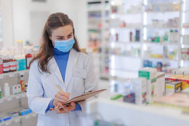 Young pharmacist checking medicine stock in a pharmacy. - HPIF11129