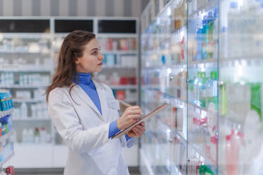 Young pharmacist checking medicine stock in a pharmacy. - HPIF11130