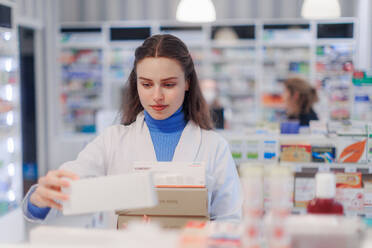 Young pharmacist checking medicine stock in a pharmacy. - HPIF11133