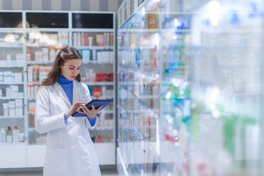 Young pharmacist checking medicine stock in a pharmacy. - HPIF11134