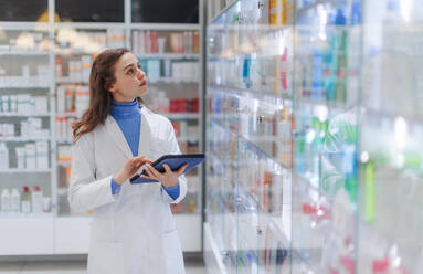 Young pharmacist checking medicine stock in a pharmacy. - HPIF11135