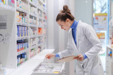 Young pharmacist checking medicine stock in a pharmacy. - HPIF11138