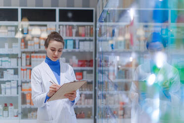 Young pharmacist checking medicine stock in a pharmacy. - HPIF11146