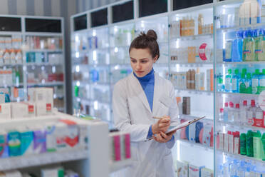 Young pharmacist checking medicine stock in a pharmacy. - HPIF11151