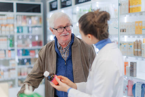 Eine junge Apothekerin hilft einem älteren Mann bei der Auswahl eines Medikaments. - HPIF11153