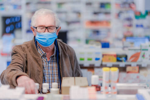 Ein älterer Mann wählt in einer Apotheke Medikamente aus. - HPIF11162