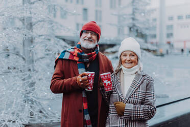 Ein glückliches älteres Paar genießt den Weihnachtsmarkt im Freien und trinkt Glühwein. - HPIF11166