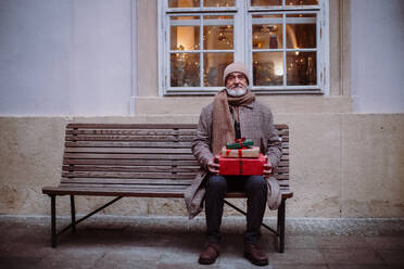 Senior man sitting alone on a bench, holding Chrismtas gifts. - HPIF11175
