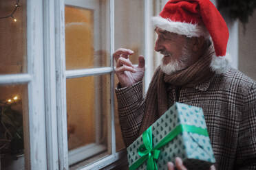 Ein älterer Mann bringt Geschenke und klopft an ein Fenster. - HPIF11176