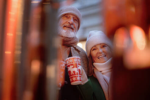 Happy senior couple enjoying outdoor christmas market, drinking punch. - HPIF11180