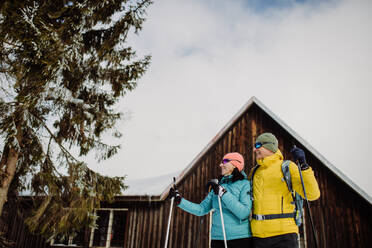 Älteres Paar macht Pause beim Skifahren, neben Wald verschneite Hütte. - HPIF11211