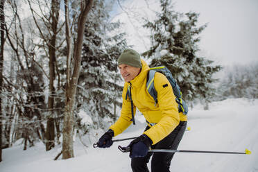 Älterer Mann beim Skilanglauf vor einem verschneiten Wald. - HPIF11251