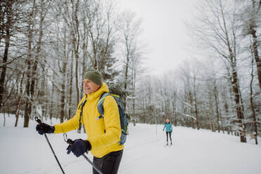 Älterer Mann beim Skilanglauf vor einem verschneiten Wald. - HPIF11252