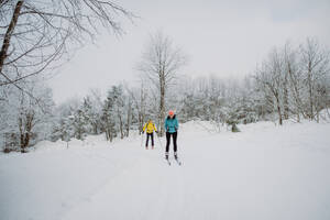 Älteres Paar beim gemeinsamen Skifahren inmitten eines verschneiten Waldes - HPIF11254