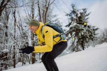 Älterer Mann beim Skilanglauf vor einem verschneiten Wald. - HPIF11255