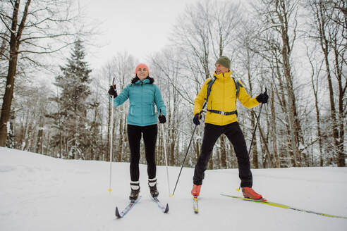 Älteres Paar beim gemeinsamen Skifahren inmitten eines verschneiten Waldes - HPIF11258