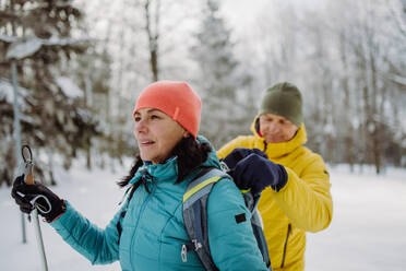 Älteres Paar beim gemeinsamen Skifahren inmitten eines verschneiten Waldes, das eine Pause einlegt. - HPIF11259