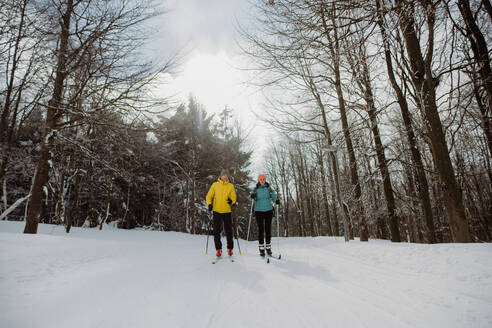 Älteres Paar beim gemeinsamen Skifahren inmitten eines verschneiten Waldes - HPIF11262