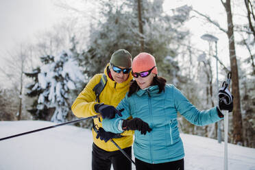 Senior couple looking at a smartwatch during winter skiing. - HPIF11280