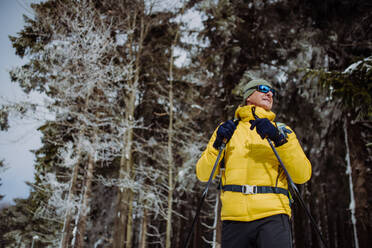 Low angle view of senior man admiring nature during cross country skiing in forest. - HPIF11283