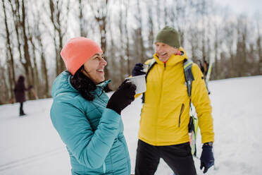 Senior couple resting and drinking hot tea from thermos in the middle of snowy forest. - HPIF11291