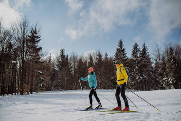 Älteres Paar beim Skifahren inmitten eines verschneiten Waldes. - HPIF11297