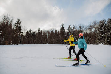 Älteres Paar beim gemeinsamen Skifahren inmitten eines verschneiten Waldes - HPIF11302