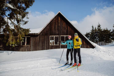 Senior couple having break during skying, next forest snowy cottage. - HPIF11308