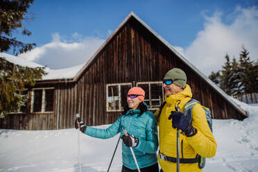 Senior couple having break during skying, next forest snowy cottage. - HPIF11309