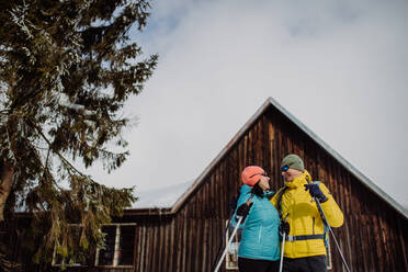 Älteres Paar macht Pause beim Skifahren, neben Wald verschneite Hütte. - HPIF11310