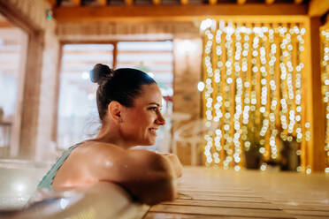 Junge Frau genießt an einem kalten Winterabend eine Badewanne auf ihrer Terrasse. - HPIF11342