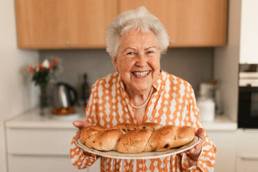 Glückliche ältere Frau mit selbstgebackenem süßem Zopfbrot mit Rosinen. - HPIF11348