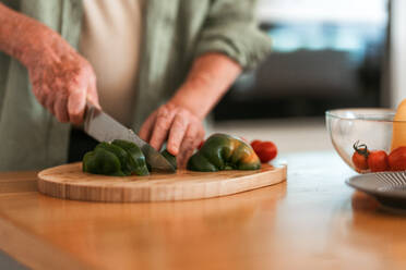 Nahaufnahme eines älteren Mannes bei der Zubereitung von Gemüse, Schneiden auf einem Holzbrett, Konzept der gesunden Lebensweise. - HPIF11354