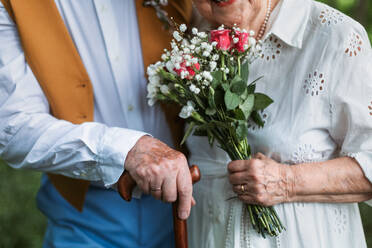 Nahaufnahme von Seniorenhänden mit Brautstrauß und goldenen Eheringen während ihrer Hochzeit. - HPIF11400