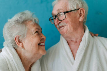Porträt eines glücklichen älteren Paares, das zusammen im Bademantel auf dem Sofa sitzt und eine schöne Zeit zu Hause hat. - HPIF11428