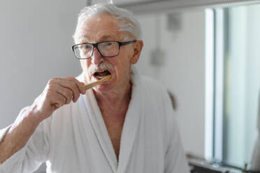 Älterer Mann putzt sich die Zähne mit einer Holzbürste im Badezimmer, nachhaltiger Lebensstil. - HPIF11437