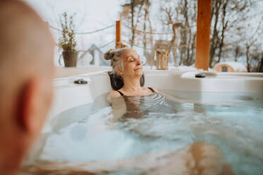 Ältere Frau genießt mit ihrem Mann an einem kalten Wintertag eine Badewanne auf der Terrasse. - HPIF11466